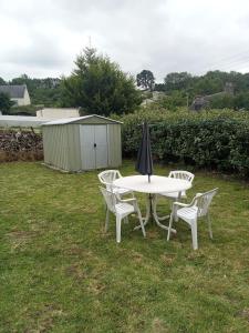 une table blanche avec deux chaises et un parasol dans l'établissement Ti an traõn le petit gîte en cœur de Bretagne, à Carhaix-Plouguer
