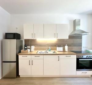 eine Küche mit weißen Schränken und einem Edelstahlkühlschrank in der Unterkunft Modernes Apartment mit Queensize-Bett, NETFLIX, Küche, Erdgeschoss, Nähe AMEOS Klinik in Aschersleben
