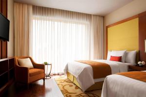 a hotel room with two beds and a chair and a window at Courtyard by Marriott Kochi Airport in Nedumbassery