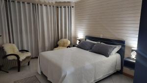 a bedroom with a white bed and two chairs at Super Casa de 3 Quartos ao Lado da Igreja Matriz in Urubici