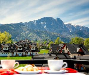 a table with plates of food on a balcony with mountains at Grand Podhale Resort&Spa Zakopane - Jacuzzi - Sauna fińska i Łaźnia parowa - Widok na Tatry in Zakopane