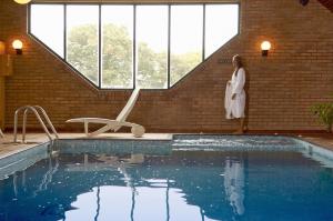 a woman in a white robe standing next to a swimming pool at Passford House Hotel in Lymington
