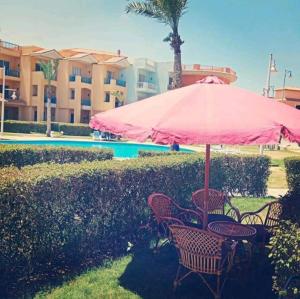 a table and chairs with a pink umbrella next to a pool at Porto Matroh Eid in Marsa Matruh