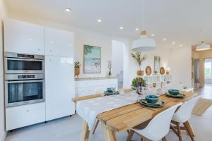 a white kitchen with a wooden table and white appliances at Szabadi Pihenőház by BLTN in Siófok