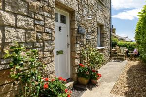 a stone house with a white door and flowers at Mousehole Cottage in Penzance
