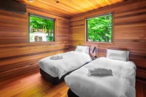two beds in a room with wooden walls and windows at Phoenix Chalets by HHG in Hakuba +37 photos