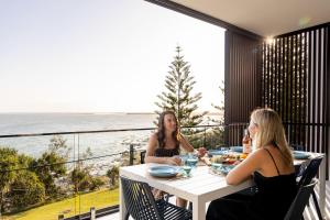 two women sitting at a table on a balcony with the ocean at Kings Beach Oceanfront Oasis in Caloundra +39 photos