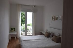 a white bedroom with a bed and a window at Apartments Fink in Portorož