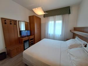 a bedroom with a white bed and a television at Hotel Alla Dolina in Sistiana