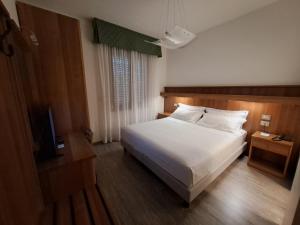 a bedroom with a white bed and a television at Hotel Alla Dolina in Sistiana