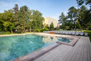 a swimming pool with chairs and a building in the background at Hunguest Helios Hévíz in Hévíz