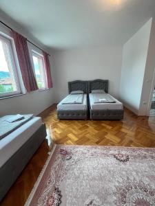 Dos camas en una habitación con suelo de madera y ventanas. en Villa Holiday, en Bihać