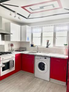 a kitchen with red cabinets and a washing machine at Westfield Gardens - 3 Bedroom Apartment in Goodmayes
