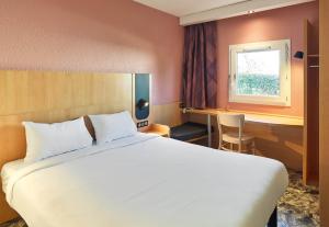 een slaapkamer met een groot wit bed en een raam bij B&B HOTEL Orly Rungis Aéroport 3 étoiles in Rungis