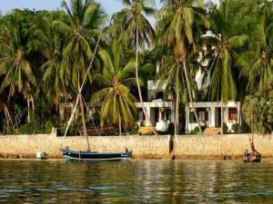 een huis met palmbomen en een boot in het water bij Jannataan Hotel in Lamu