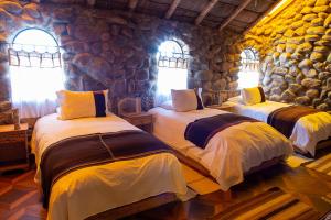 two beds in a room with a stone wall at Tambo Coquesa Lodge in Coquesa