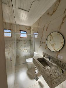 une salle de bain avec un lavabo, des toilettes et un miroir dans l'établissement Ninho dos Pássaros Chalés, à Monte Verde