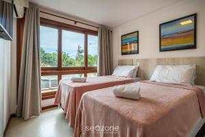 two beds in a room with a large window at CPR - Apartamentos a 200m da praia com Piscina in Marau