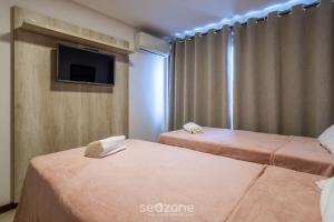 two beds in a room with a tv on the wall at CPR - Apartamentos a 200m da praia com Piscina in Marau