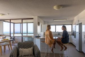 two women are sitting in a kitchen with a counter at Breezy Kings Beach Apartment with Ocean Views in Caloundra