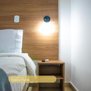 a bedroom with a bed and a nightstand with a light on the wall at Bela Vista Hotel in Arujá