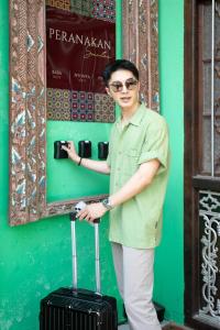 a man standing next to a green wall with a suitcase at Peranakan Suites Georgetown in George Town