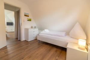 a white bedroom with a bed and a dresser at Deichblick No1 in Krummhörn