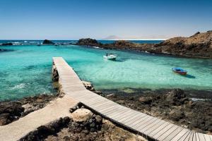 a wooden pathway in the water with two boats at Apartamento Verdemare in Corralejo