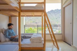 un hombre sentado en una cama en una habitación con literas en Perfectstayz Value Alpine Retreat, en Rishīkesh