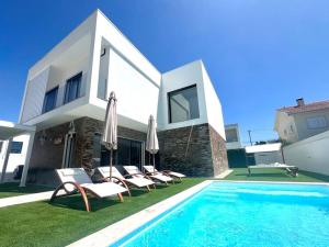 a villa with a swimming pool with chairs and umbrellas at Casa Charli Lisboa-Piscine chauffée en option in Aroeira