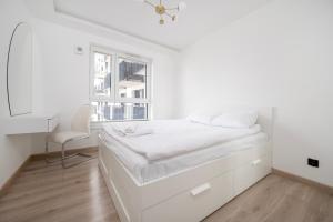 a white bedroom with a bed and a window at Widzewska Deluxe Apartment by BookingHost in Łódź