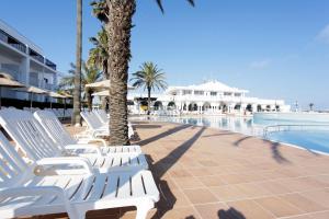 a row of white lounge chairs next to a swimming pool at Grupotel Mar de Menorca in Es Canutells