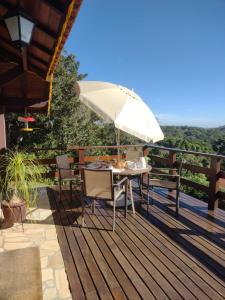 a table and chairs on a deck with an umbrella at Chalé Recanto Bela Vista in Monte Verde