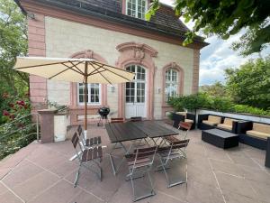 Un patio con una mesa y sillas y una sombrilla. en Teehaus im Schlosspark Weltkulturerbe Corvey, en Höxter