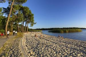a group of people sitting on a beach next to the water at Maison climatisée proche du lac in Sanguinet