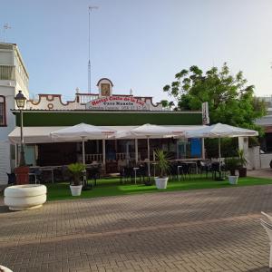 restauracja z białymi parasolami, stołami i krzesłami w obiekcie Hostal Costa de la Luz w mieście Chipiona