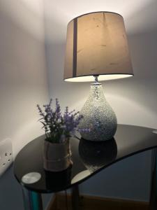 una mesa con una lámpara y un jarrón con flores púrpuras en The ComfortGrove Apartment, en Mánchester