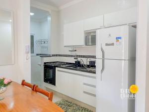 a white kitchen with a table and a refrigerator at Top das Toninhas – Apto c/ Ar e Vista Mar e roupa de cama in Ubatuba