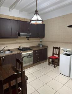 Una cocina con gabinetes marrones, una mesa y un refrigerador. en Résidence Oubaha - Grand appartement avec piscine, en Mohammedia