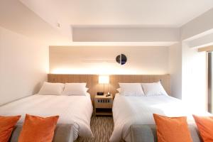 two beds in a room with white walls and orange pillows at AoAwo Naruto Resort in Naruto