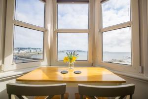 ein Esszimmer mit einem Tisch und drei Fenstern in der Unterkunft St Georges Guest House in St Peter Port