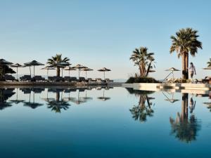 a pool of water with palm trees and umbrellas at Cora Hotel & Spa in Afitos