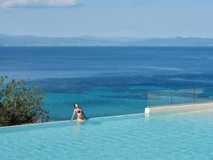 a woman standing in a swimming pool overlooking the ocean at Cora Hotel & Spa in Afitos