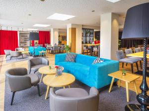 Un vestíbulo con un sofá azul, mesas y sillas. en JUFA Hotel Salzburg, en Salzburgo
