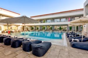 a pool with chairs and umbrellas next to a building at White Olive Premium Laganas in Laganas