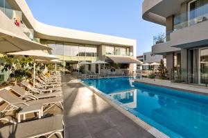a swimming pool with chairs and umbrellas next to a building at White Olive Premium Laganas in Laganas