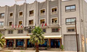 un grande edificio grigio con una palma di fronte di Hôtel AL QAISAR a Er Rachidia