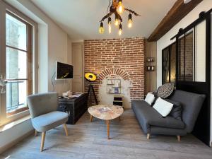 a living room with a couch and chairs and a brick wall at Côté Médicis - Cosy appartement au coeur de Blois in Blois