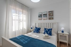 a white bedroom with a bed with blue pillows at Renovated apartment on beachside with pool in Nerja