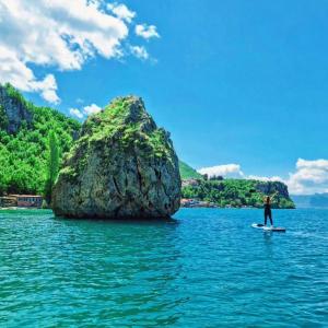 a man on a surfboard in the water near a large rock at Villa Gjorgi in Ohrid